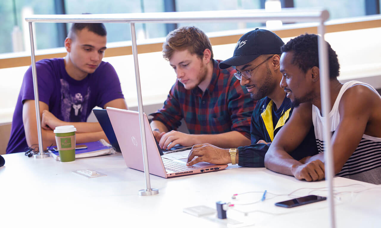 students in the library gathered around a laptop